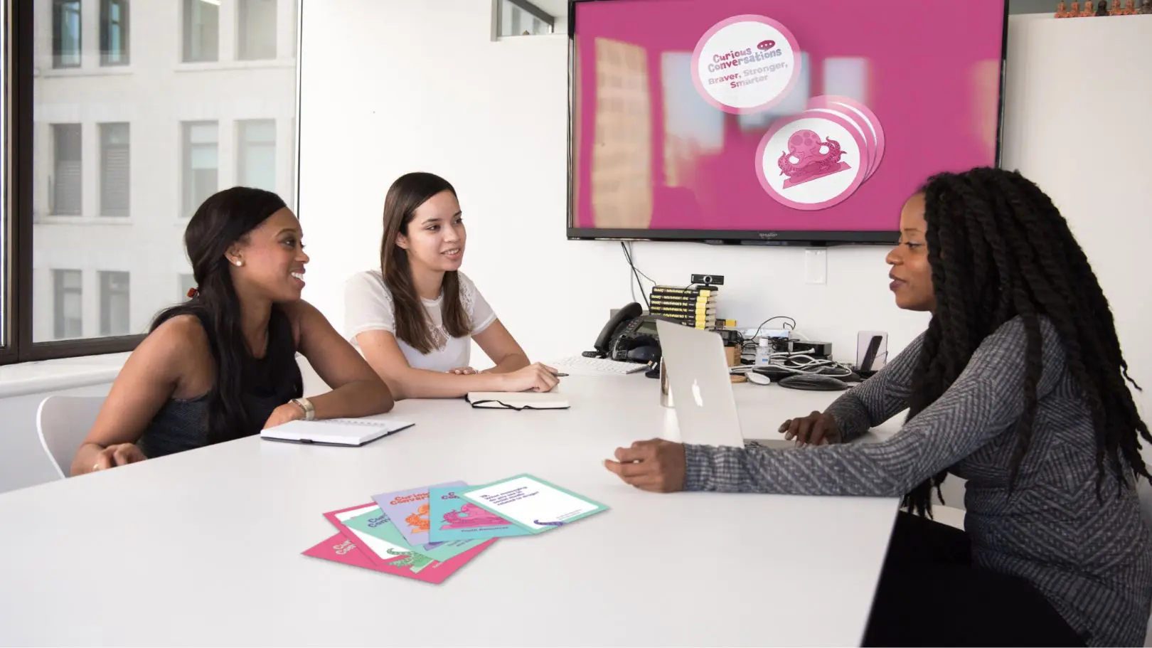 Curious Conversations cards and campaign graphic shown in a meeting room