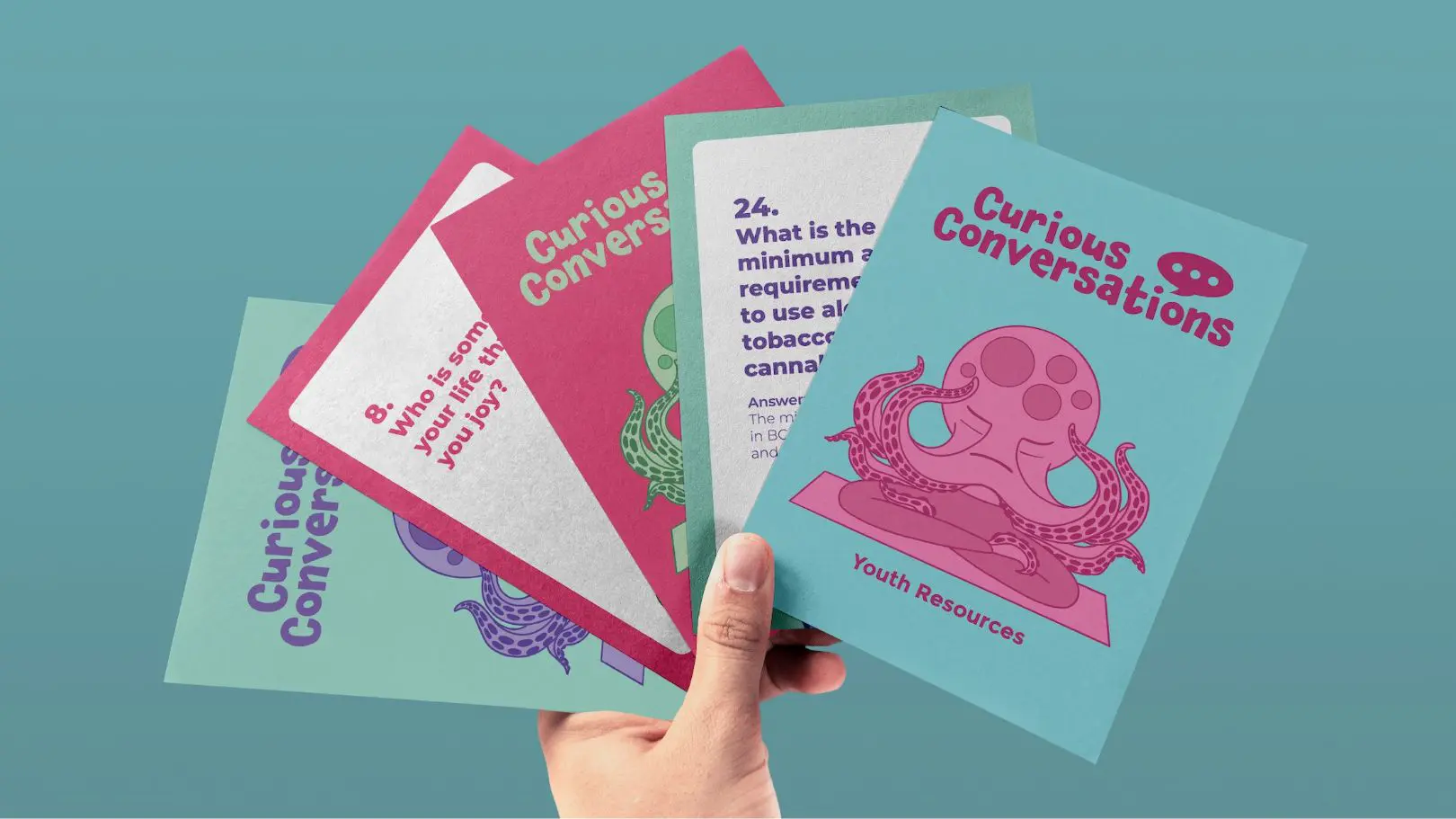 Hand holding Curious Conversations cards in multiple colours