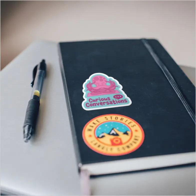 Curious Conversations sticker on notebook beside pen